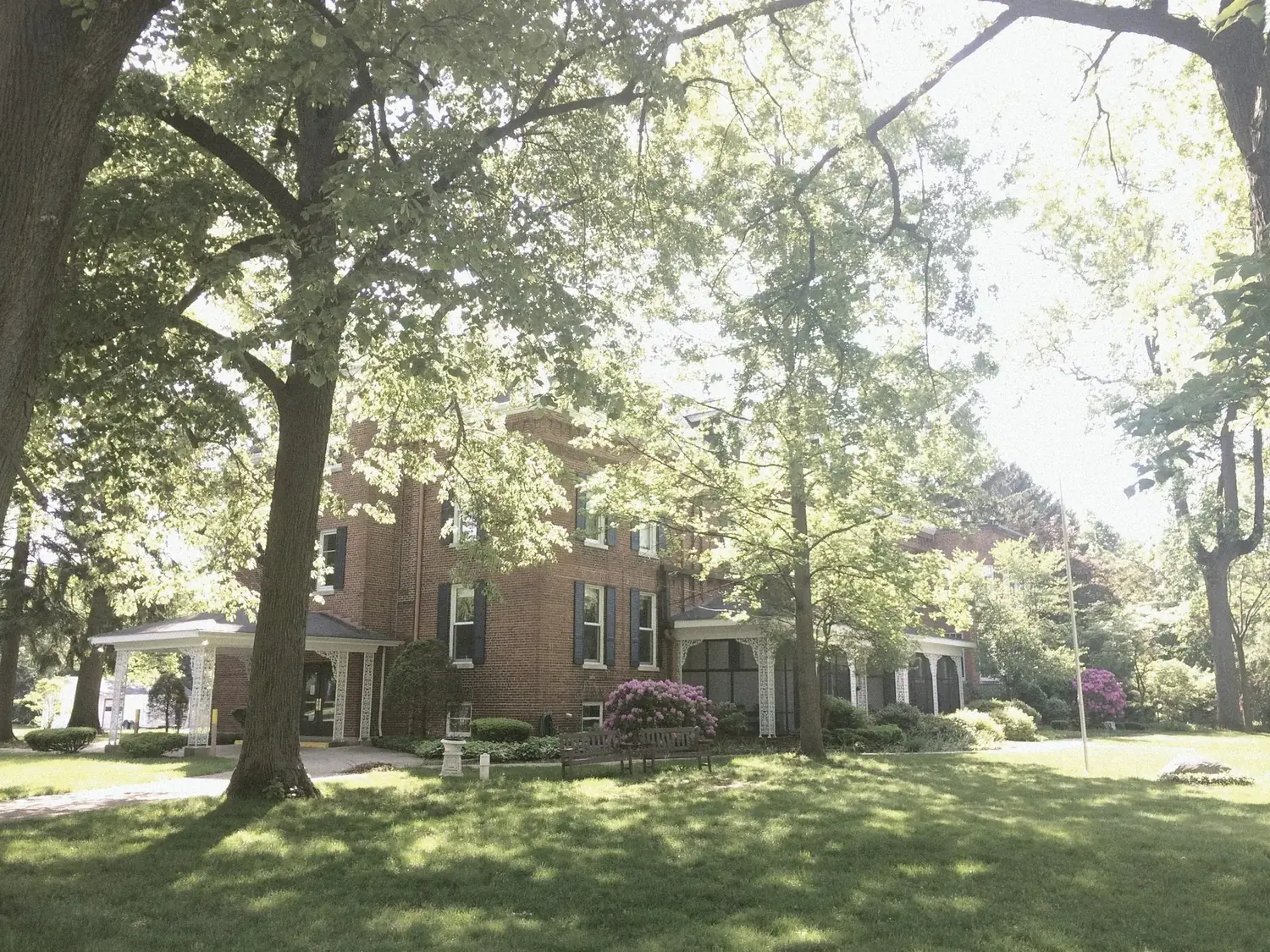 Red brick mansion through mature trees with rhododendrons in bloom