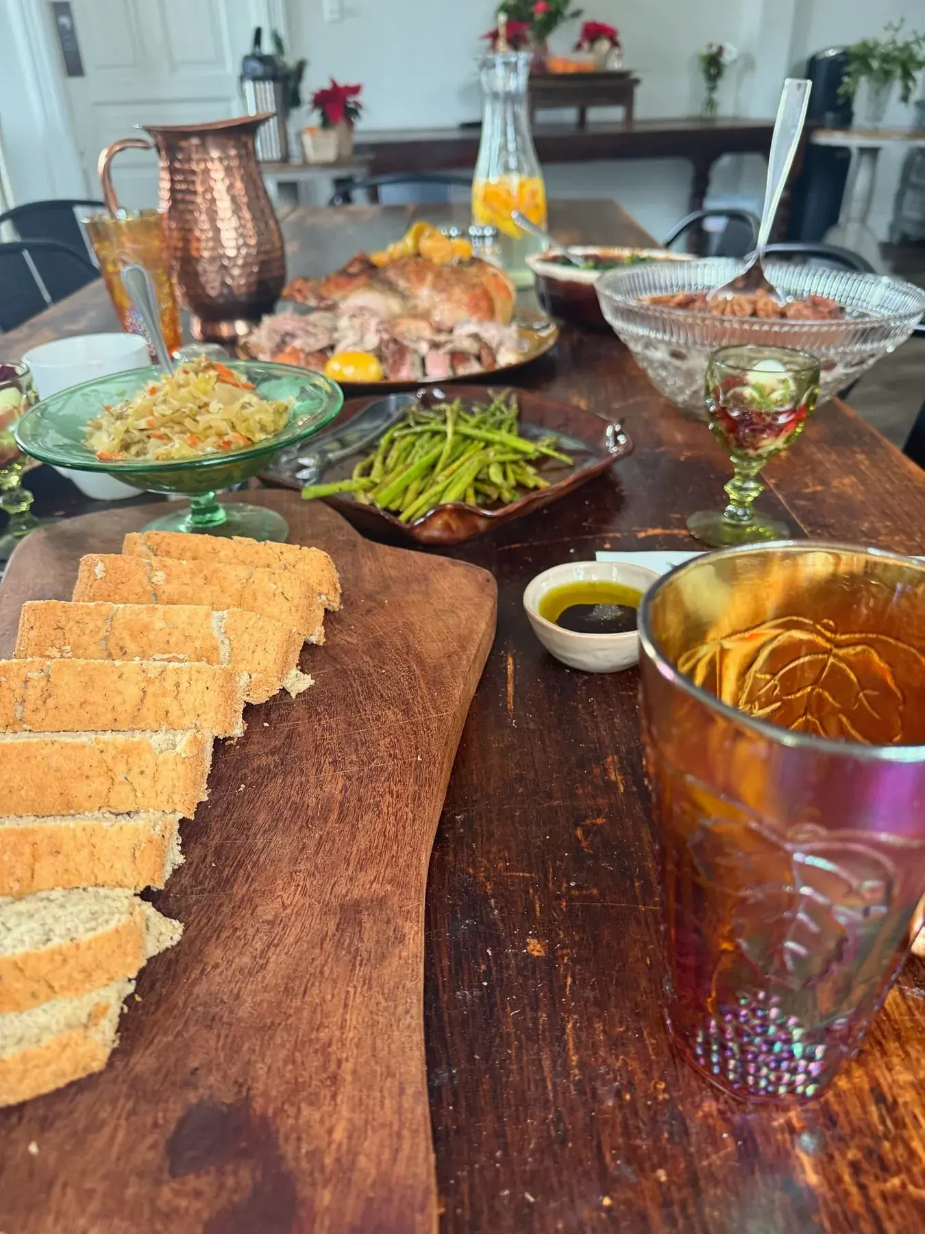 Family-style dinner spread — bread board, copper pitcher, asparagus, roasted meat